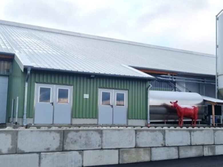 Stallgebäude von außen, rote Kuh davor